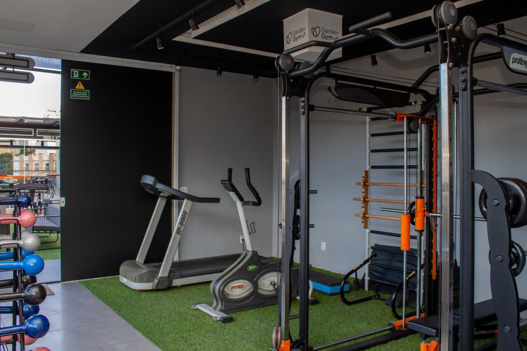 Suporte com halteres coloridos em frente a uma janela com vista para a paisagem.